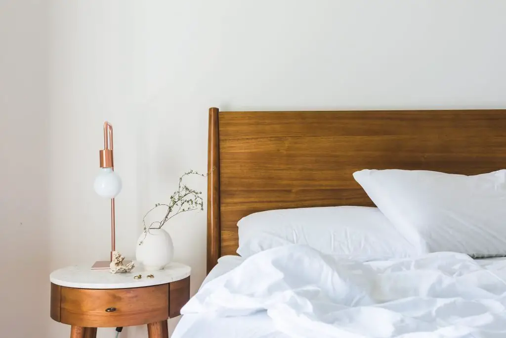 white messy sheets on a bed, bedside table with lamp and plant