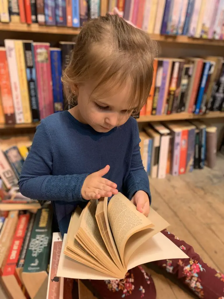 little girl flipping through pages of a book in a used book store
